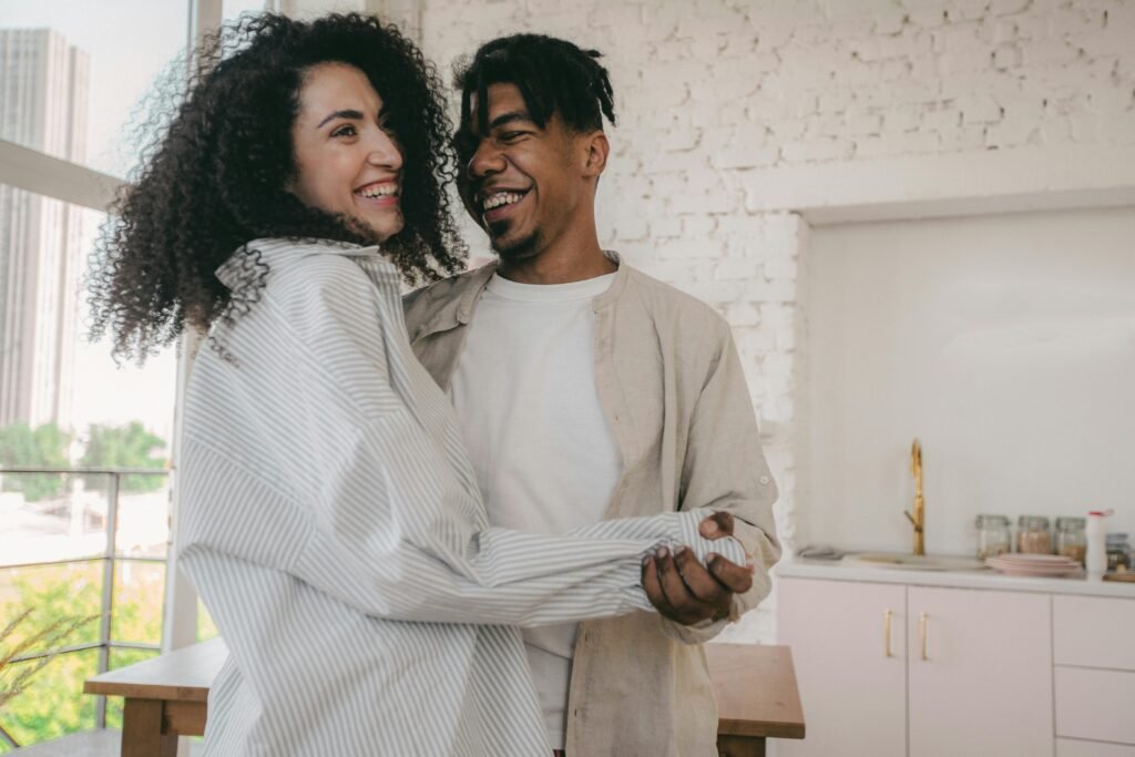Happy couple smiling and dancing together in a bright, modern kitchen setting.