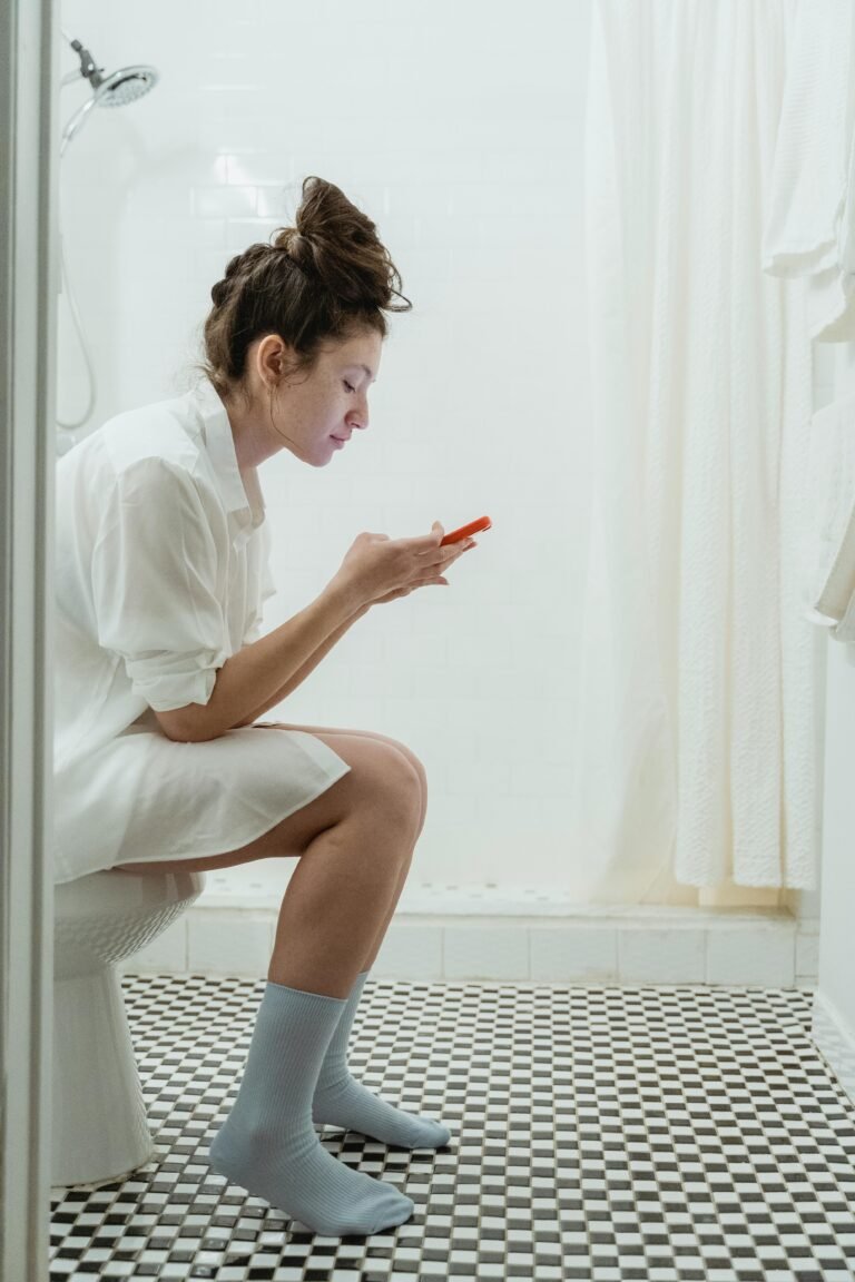 Woman in a bathroom using a smartphone while sitting on the toilet.