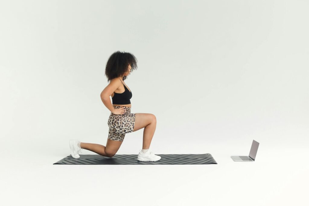 A woman doing a lunge exercise indoors with a laptop for guidance.