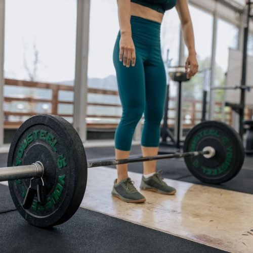 Female athlete preparing to lift a heavy barbell in a gym, showcasing fitness and strength.